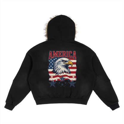 Black cropped hoodie with a faux-fur trimmed hood, shown from the back. The back features a large graphic of a bald eagle head over an American flag pattern with the word 'AMERICA' in red above it.