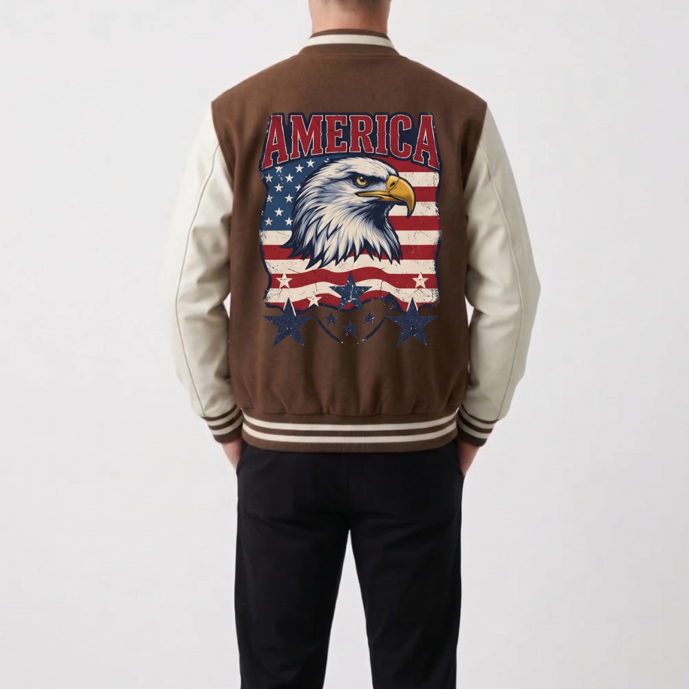 A person shown from the back wearing a brown and cream varsity-style jacket with a large American flag and bald eagle graphic on the back, paired with black pants, against a light gray studio background.