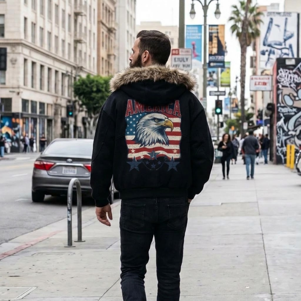 A man viewed from behind wearing a black hooded jacket with a fur-trimmed hood and a large patriotic eagle graphic on the back, standing on a city sidewalk.