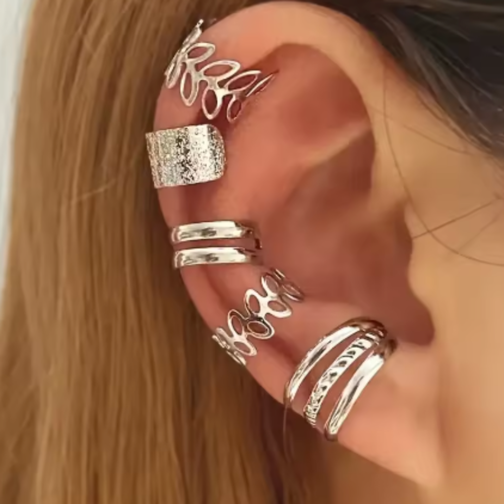 A close-up of a person's ear adorned with multiple silver-toned ear cuffs and ear rings, including a leaf-shaped cuff, a textured square-shaped cuff, and several slim curved bands.